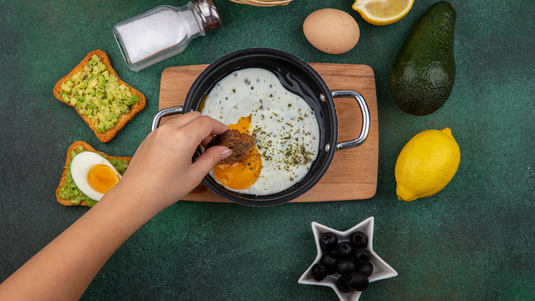 Person Prepping Meal With Eggs, Lemon, Avocado, Olives, and Salt